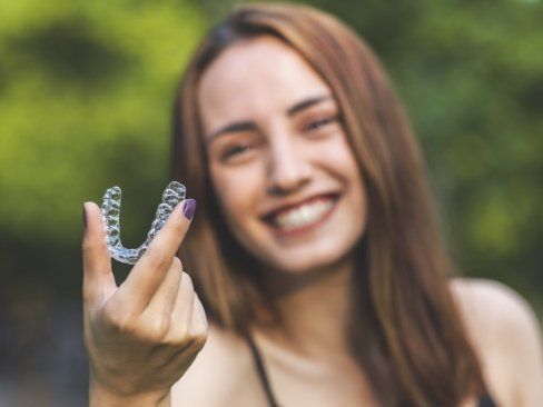 Smiling woman holding up an Invisalign clear aligner tray