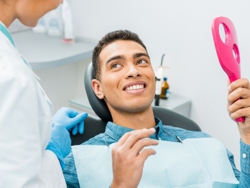 Man talking to dentist and looking at his smile in the mirror