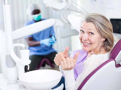 Woman smiling giving thumbs up in dental chair