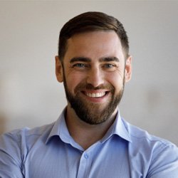 Bearded man in light blue shirt sitting and smiling