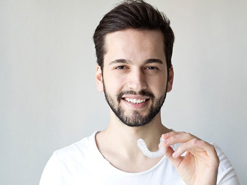 a man smiling and holding an Invisalign tray in Denver