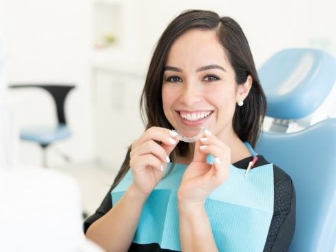 Woman in dental exam chair holding Invislaign tray