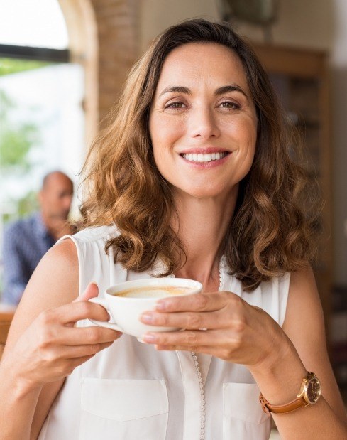 Woman holding coffee cup and smiling after preventive dentistry