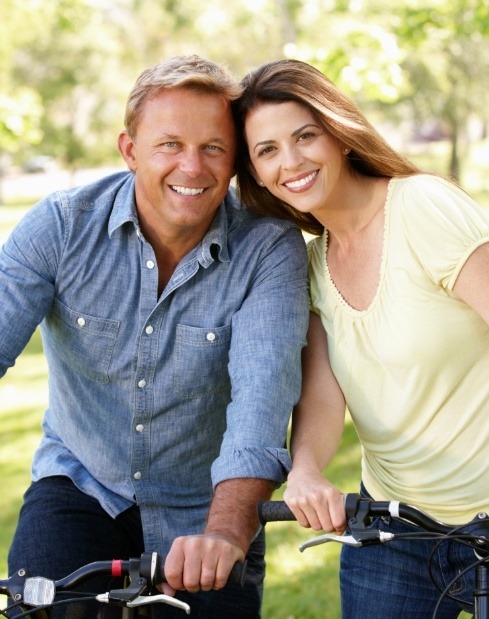 Husband and wife smiling on bikes after comprehensive dental services