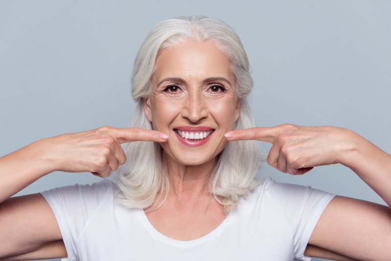 Elderly woman smiling and pointing with her index finger on each side of her face at her smile